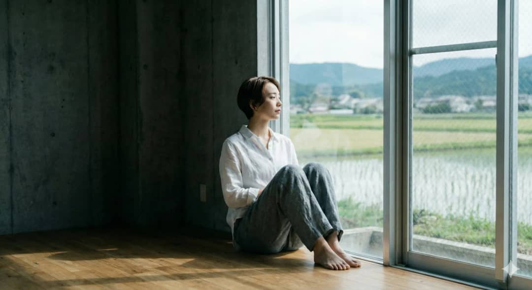 女性がものが少ない部屋の中で座って外を眺めている様子